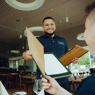 Ein Kellner mit Speisekarte im Restaurant, bereit Ihre Bestellung aufzunehmen und köstliches Essen zu servieren. Beste Restaurants am Westensee, Abendessen am Westensee.