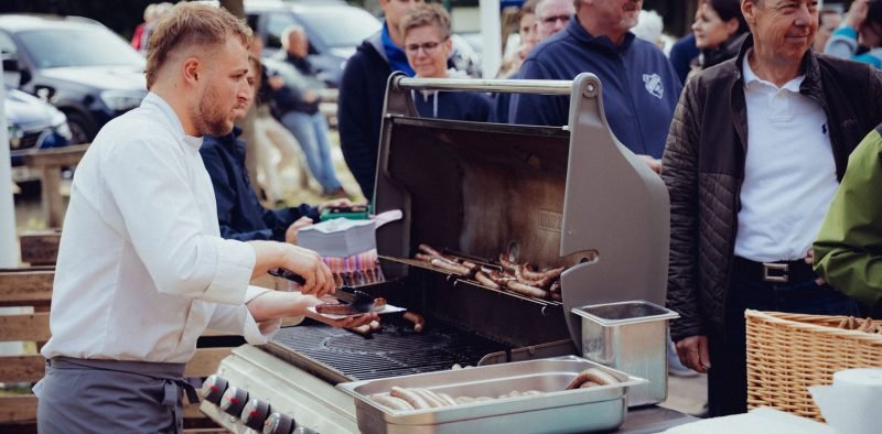 Ein Mann grillt Würstchen draußen mit Freunden. Biergarten am Westensee, Essen am Westensee.