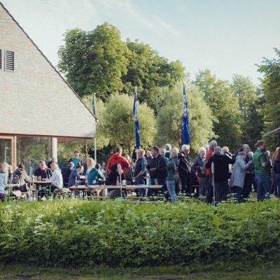 Menschen stehen vor dem Gasthaus Westensee, lächeln und unterhalten sich an einem sonnigen Tag. Veranstaltungen im Gasthaus Westensee, Restaurant für junge Leute Westensee.